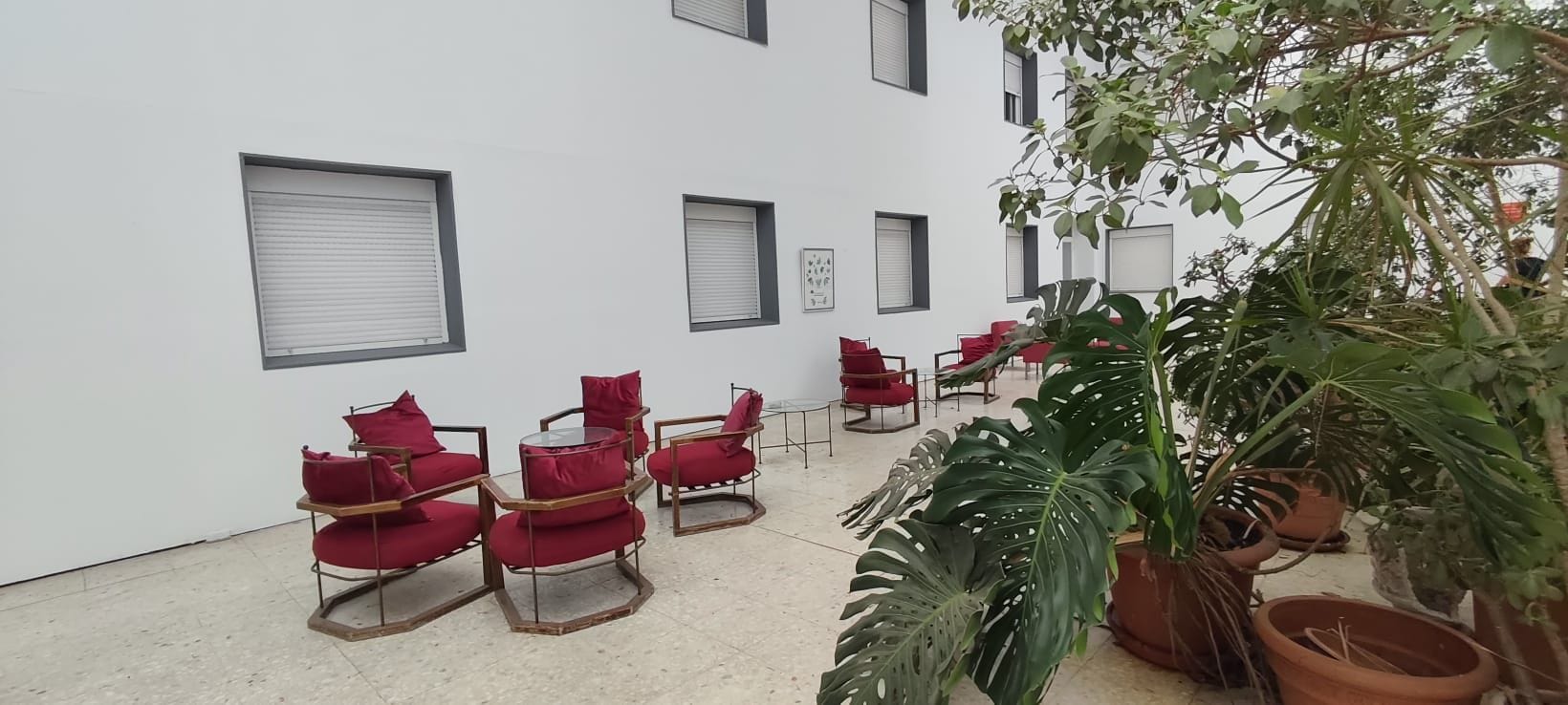 A courtyard with red chairs, potted plants, and a white building with windows.
