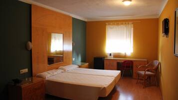 Una habitación con dos camas, un escritorio, una silla, un espejo y una ventana con cortinas.