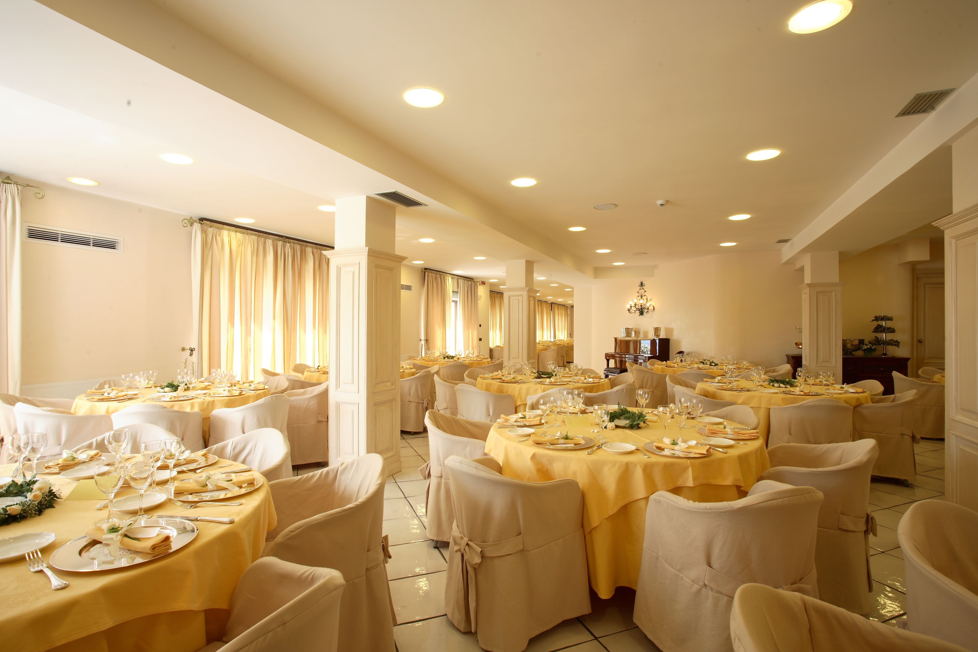 A banquet hall with round tables set for dining, white chairs, and a chandelier.