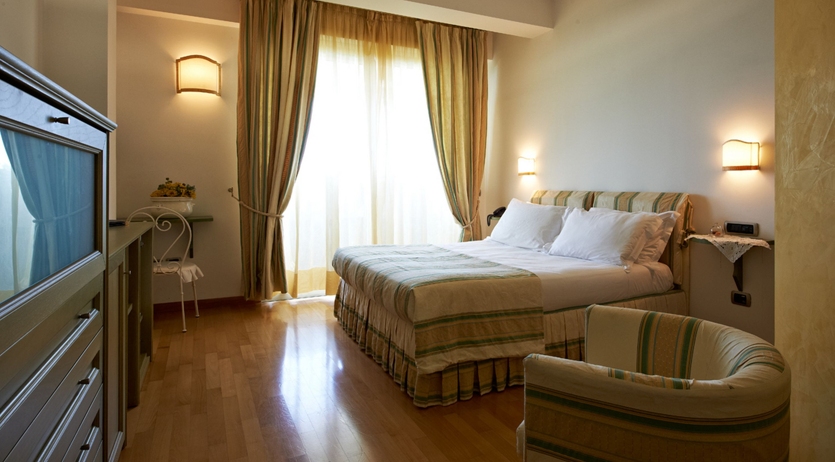 A hotel room with a bed, a chair, a desk, and a window with curtains.