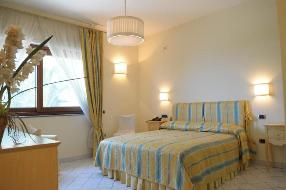 A bedroom with a bed, bedside tables, a desk, and a window with curtains.