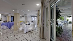 A spacious indoor dining area with multiple tables and chairs, a tiled floor, and a view of the outdoors through large windows. - Villa Poseidon Boutique Hotel & Events (Salerno)
