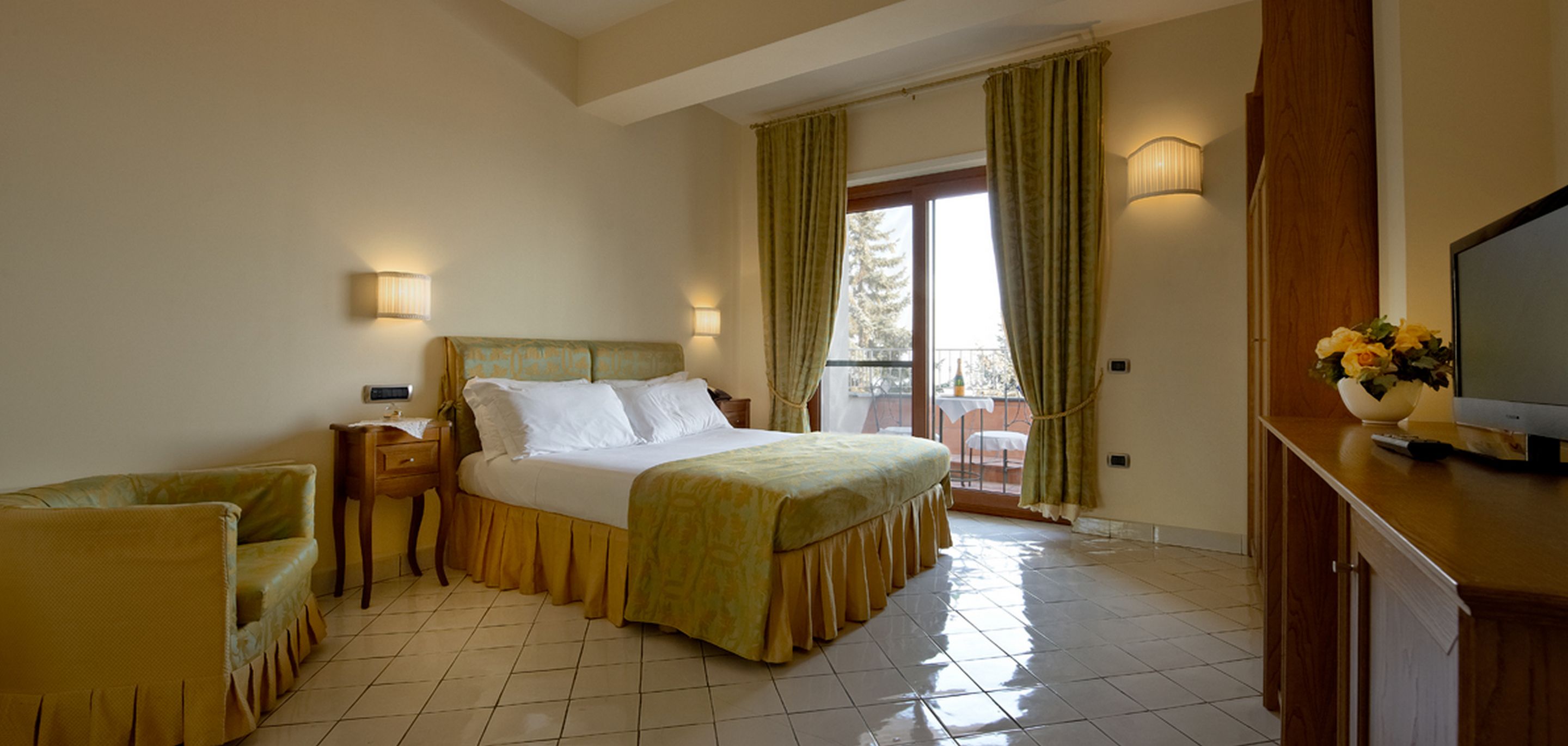 Une chambre d’hôtel avec un lit, un canapé, une télévision et un balcon avec des rideaux.