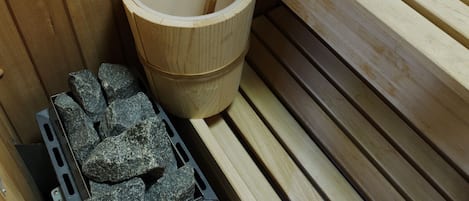 A wooden sauna with a wooden bench, a wooden bucket with a wooden mallet, and a stack of towels.