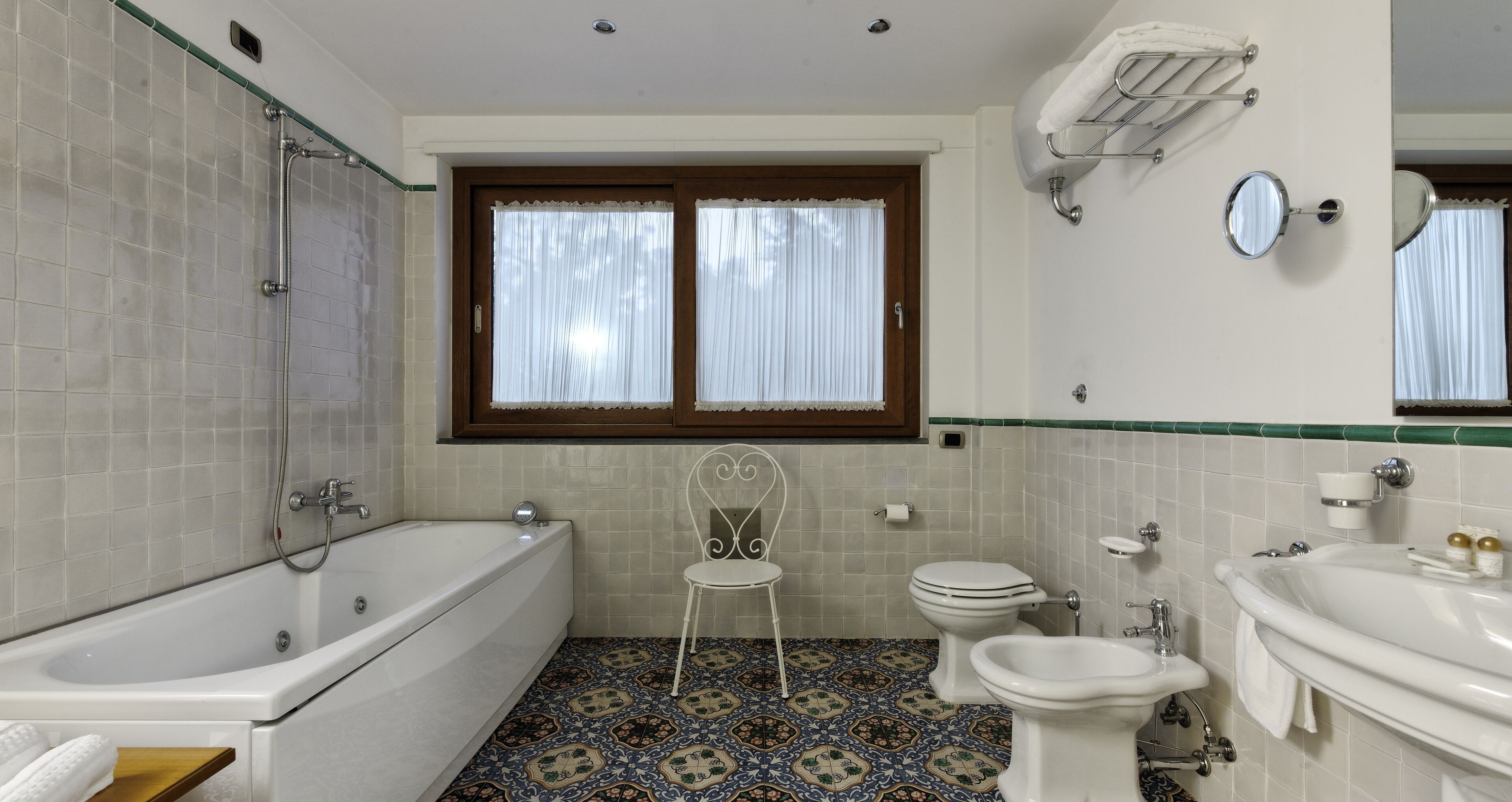 A bathroom with a bathtub, toilet, bidet, and a chair.