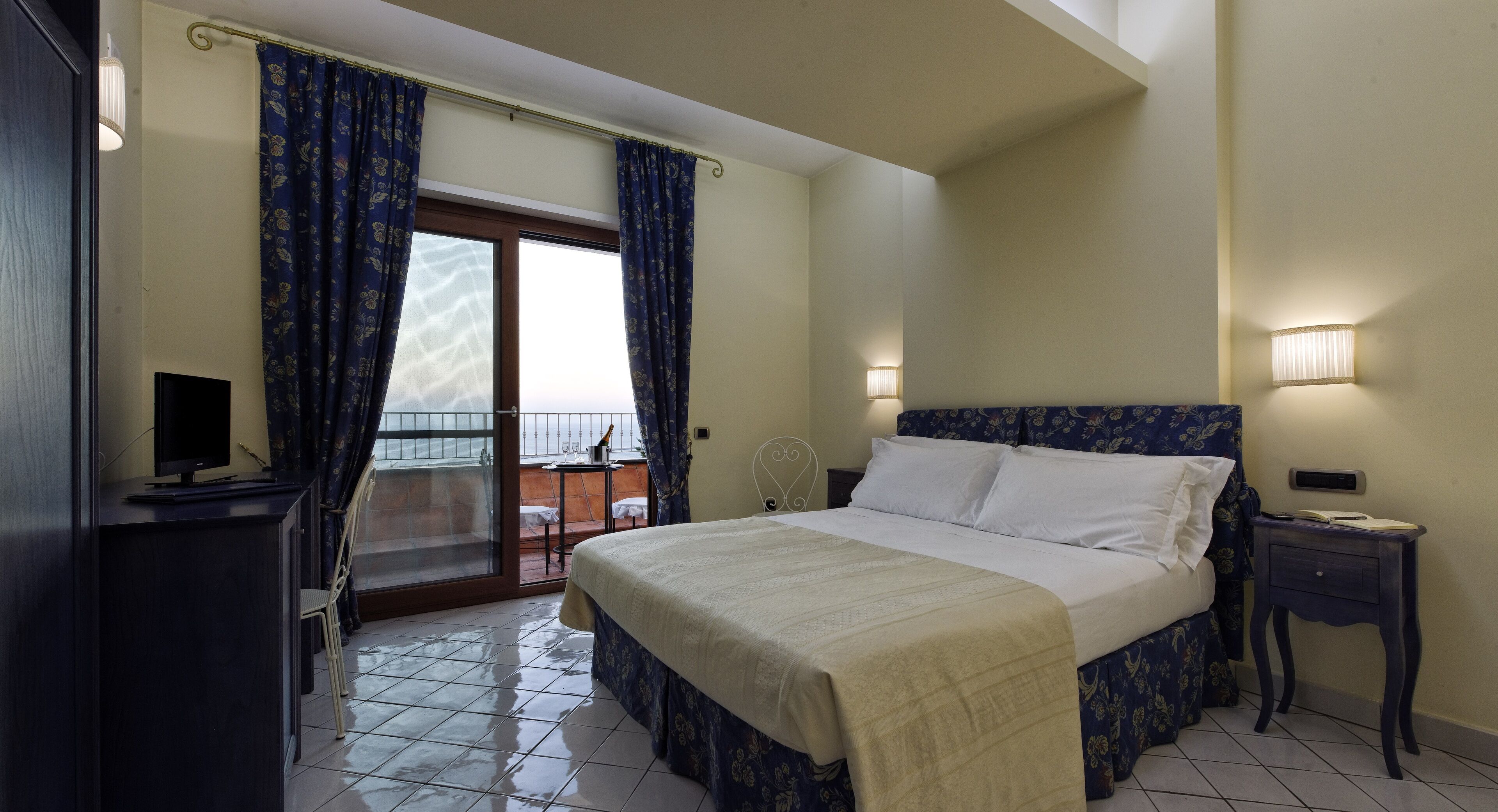A bedroom with a bed, a bedside table, a lamp, a TV, and a view through a glass door.