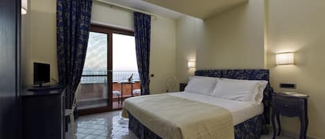 A bedroom with a bed, a bedside table, a lamp, a TV, and a view through a glass door.