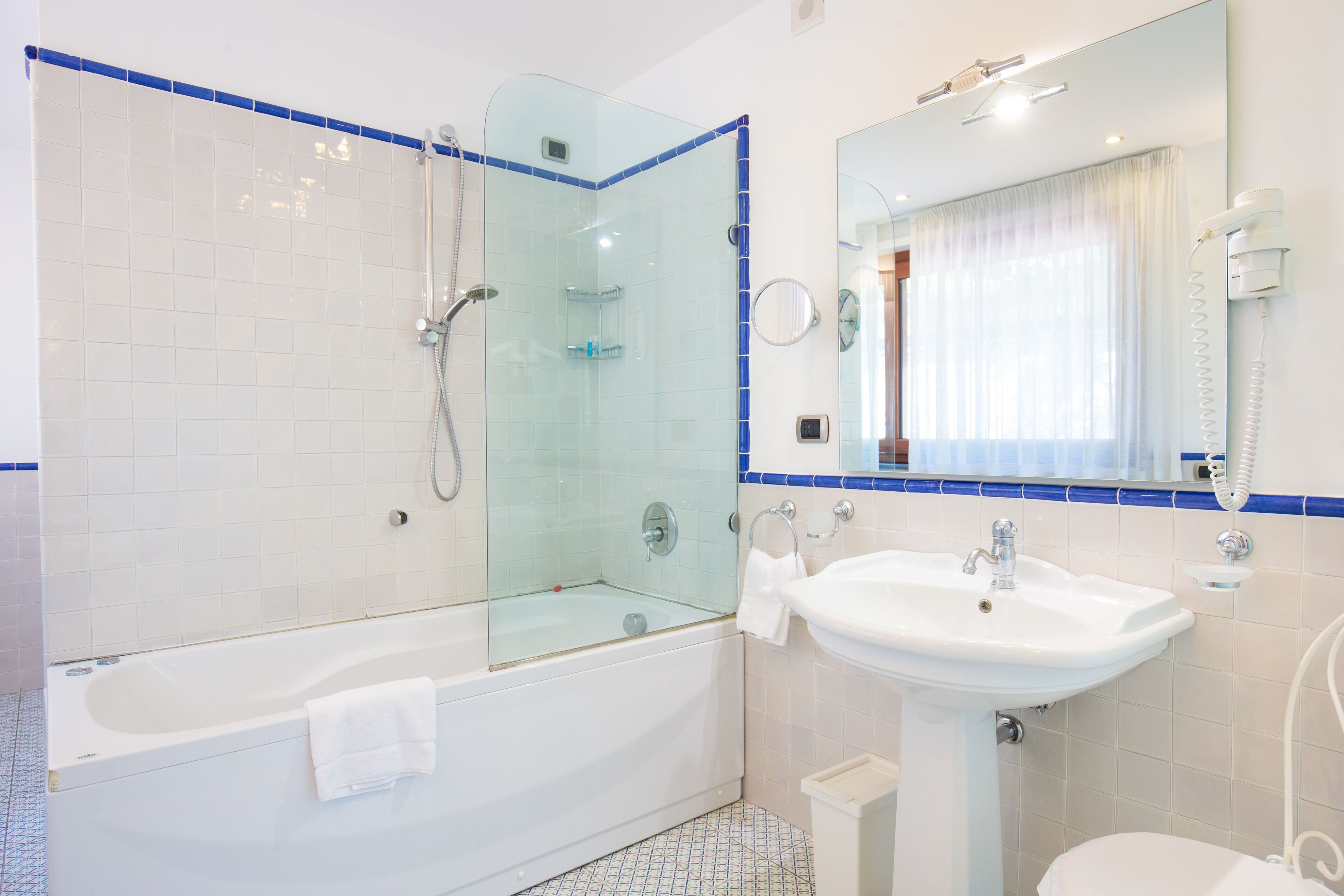 A modern bathroom with a glass-enclosed shower, a white bathtub, and a sink with a mirror above it.