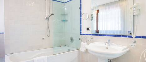 A modern bathroom with a glass-enclosed shower, a white bathtub, and a sink with a mirror above it.