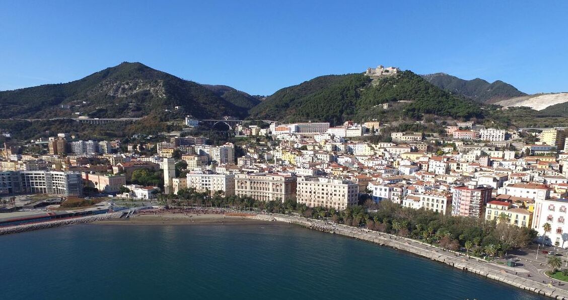 A coastal cityscape with a prominent hill and a castle-like structure on top.