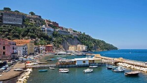 A coastal town with buildings on a hillside, a marina with boats, and a pier extending into the water. - Villa Poseidon Boutique Hotel & Events (Salerno)