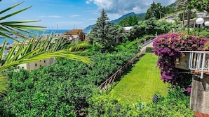 A lush garden with a pathway, a view of the sea, and buildings in the background. - Villa Poseidon Boutique Hotel & Events (Salerno)