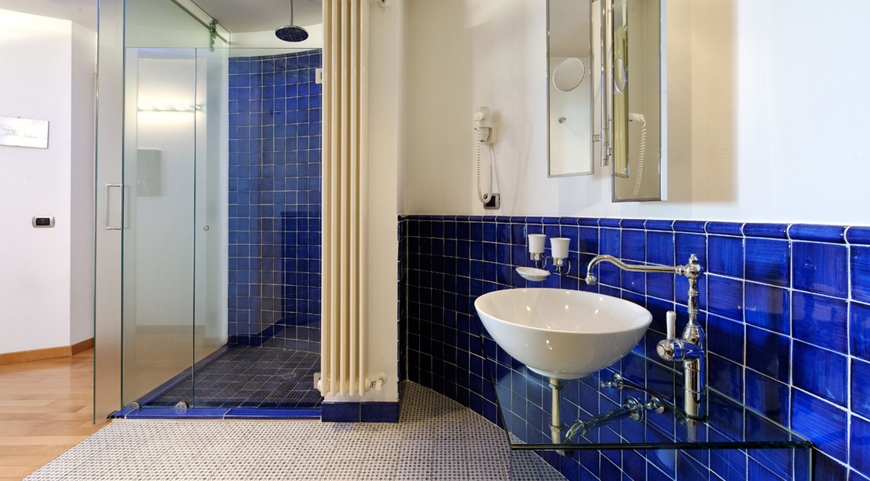 A modern bathroom with a glass shower enclosure, a white sink, and blue-tiled walls.