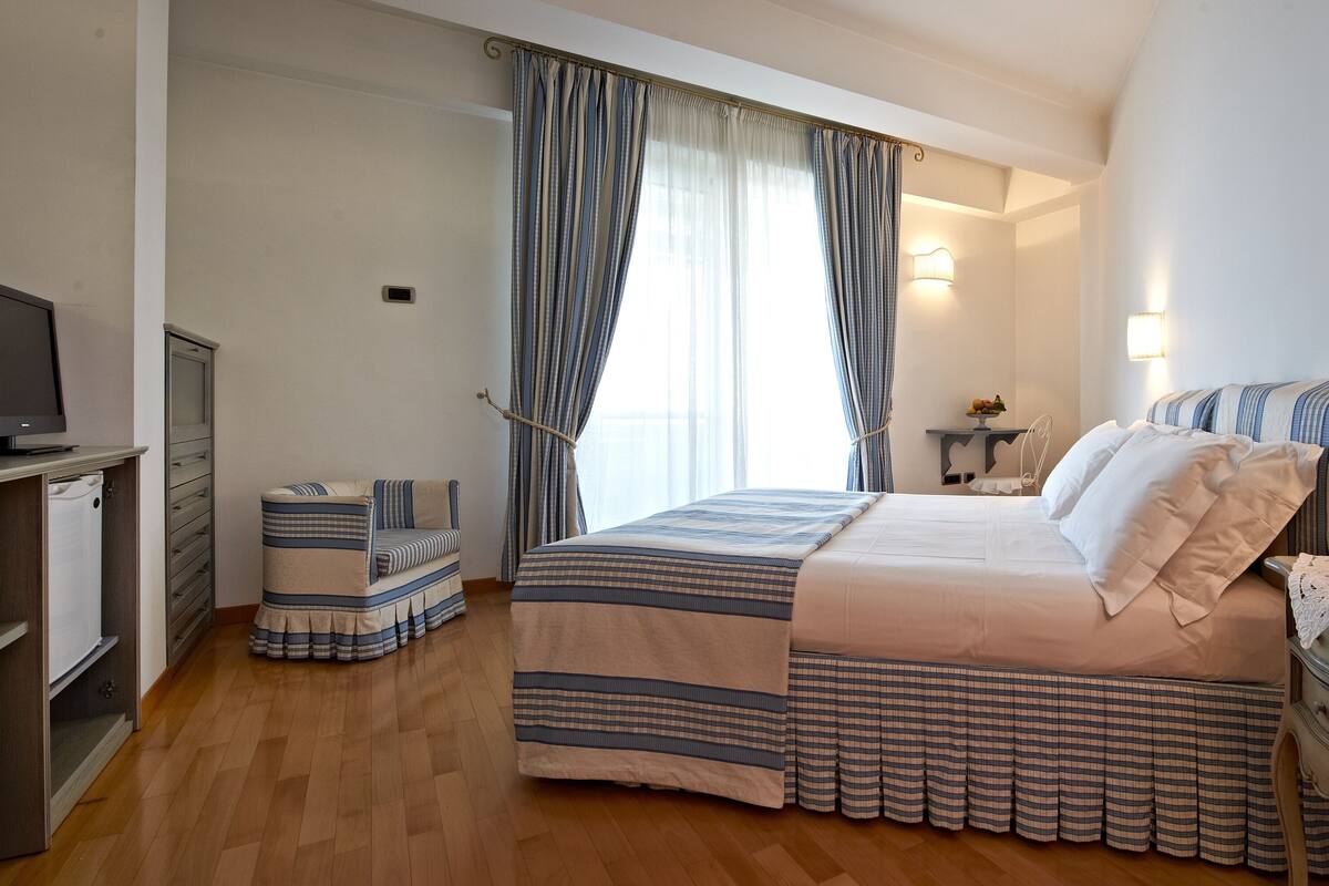A hotel room with a bed, bedside table, lamp, and a television on a stand.