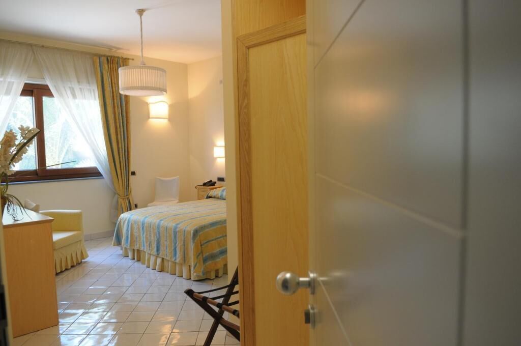 Un dormitorio con cama, mesita de noche, silla y ventana con cortinas.