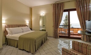A hotel room with a bed, a TV, a balcony with a view, and a chair. - Villa Poseidon Boutique Hotel & Events (Salerno)