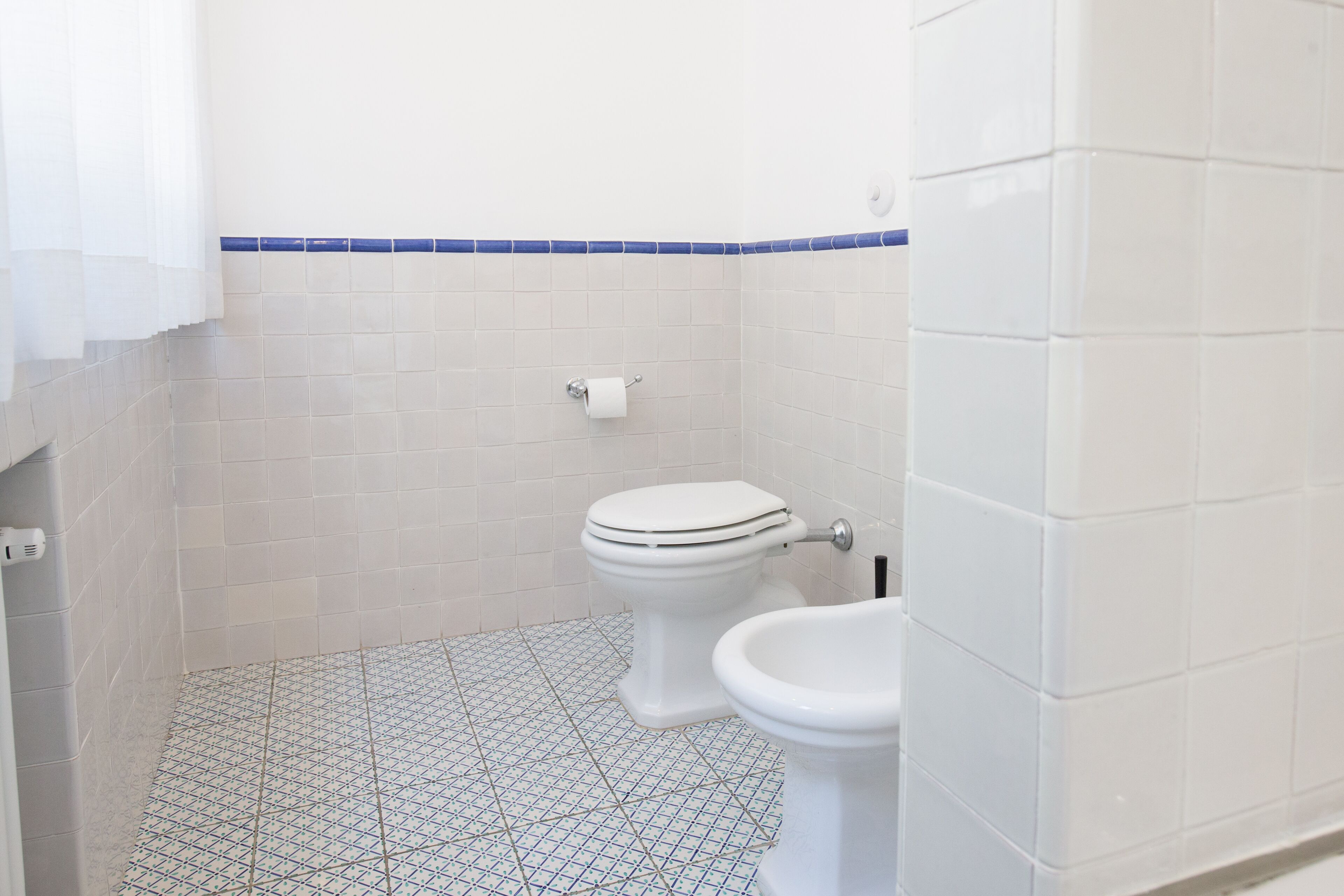 Un baño con inodoro, bidé y suelo de baldosas.