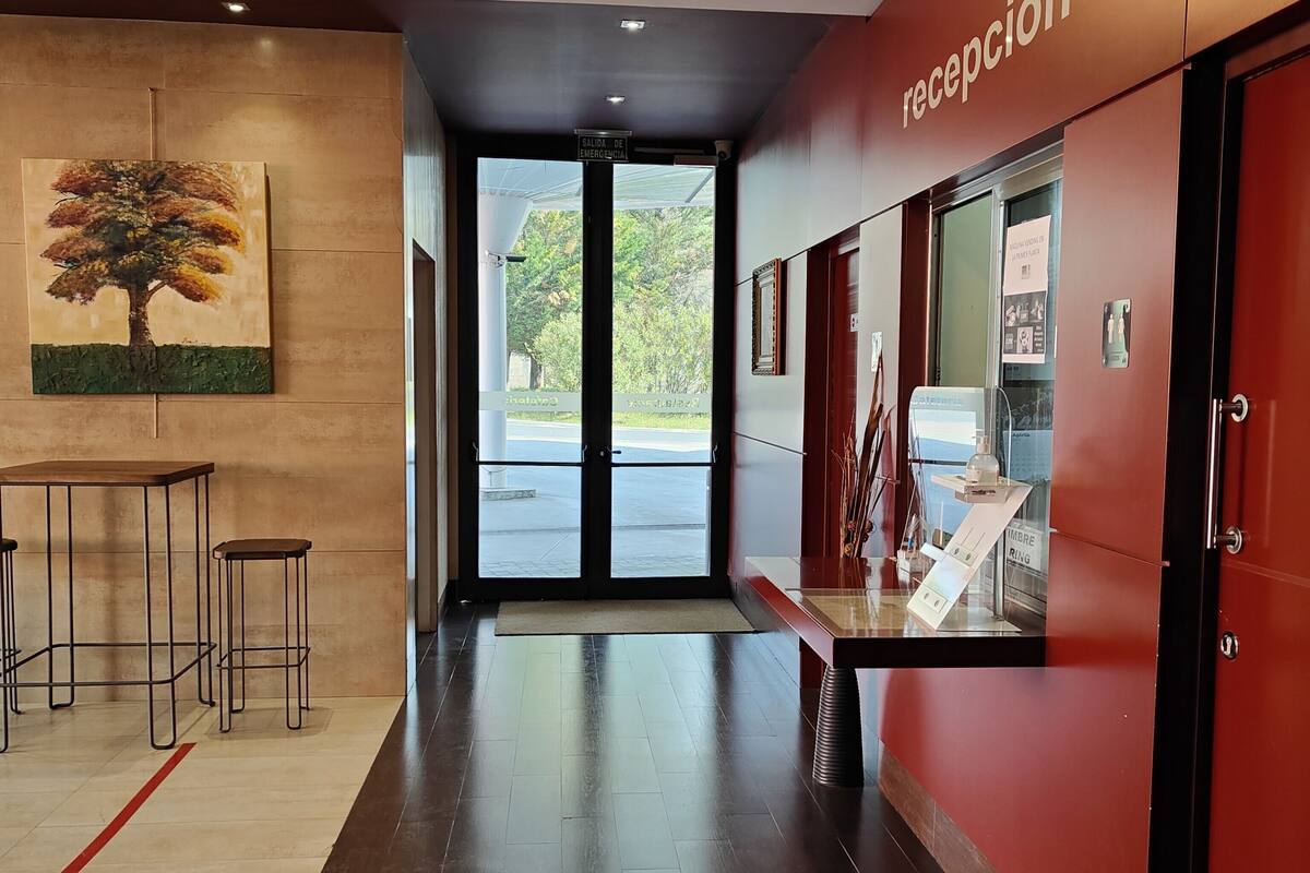 A reception area with a red wall, a glass door leading outside, and a painting of a tree on the wall.