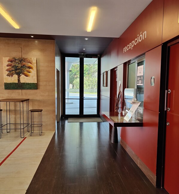 A reception area with a red wall, a glass door leading outside, and a painting of a tree on the wall. - Hotel Ortuella (Ortuella)