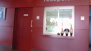 Un espace d’accueil avec un mur rouge, une fenêtre ornée de vases décoratifs et une porte portant l’inscription « accueil ».