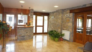 A spacious lobby with a stone wall, wooden reception desk, and a large window. - Hotel Los Nogales (Campo)