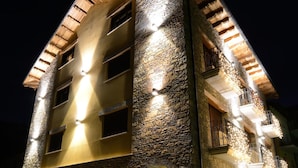 A multi-story hotel with stone facade and multiple balconies, featuring warm lighting and a visible entrance. - Hotel Los Nogales (Campo)