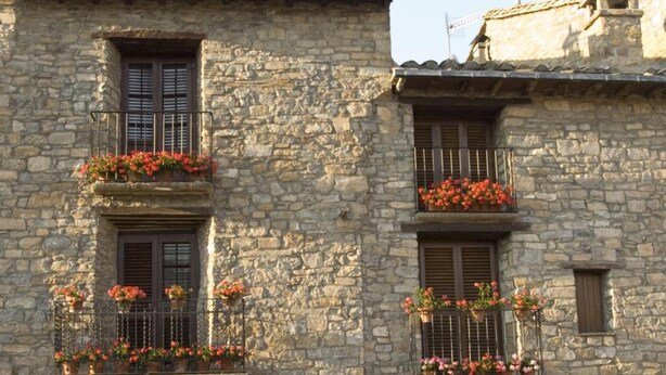 A stone building with two balconies adorned with flowers, arched doorways, and a cobblestone ground. - Hotel Los Nogales (Campo)