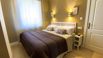 Een slaapkamer met een groot bed, twee nachtkastjes, een deur en een raam met gordijnen.