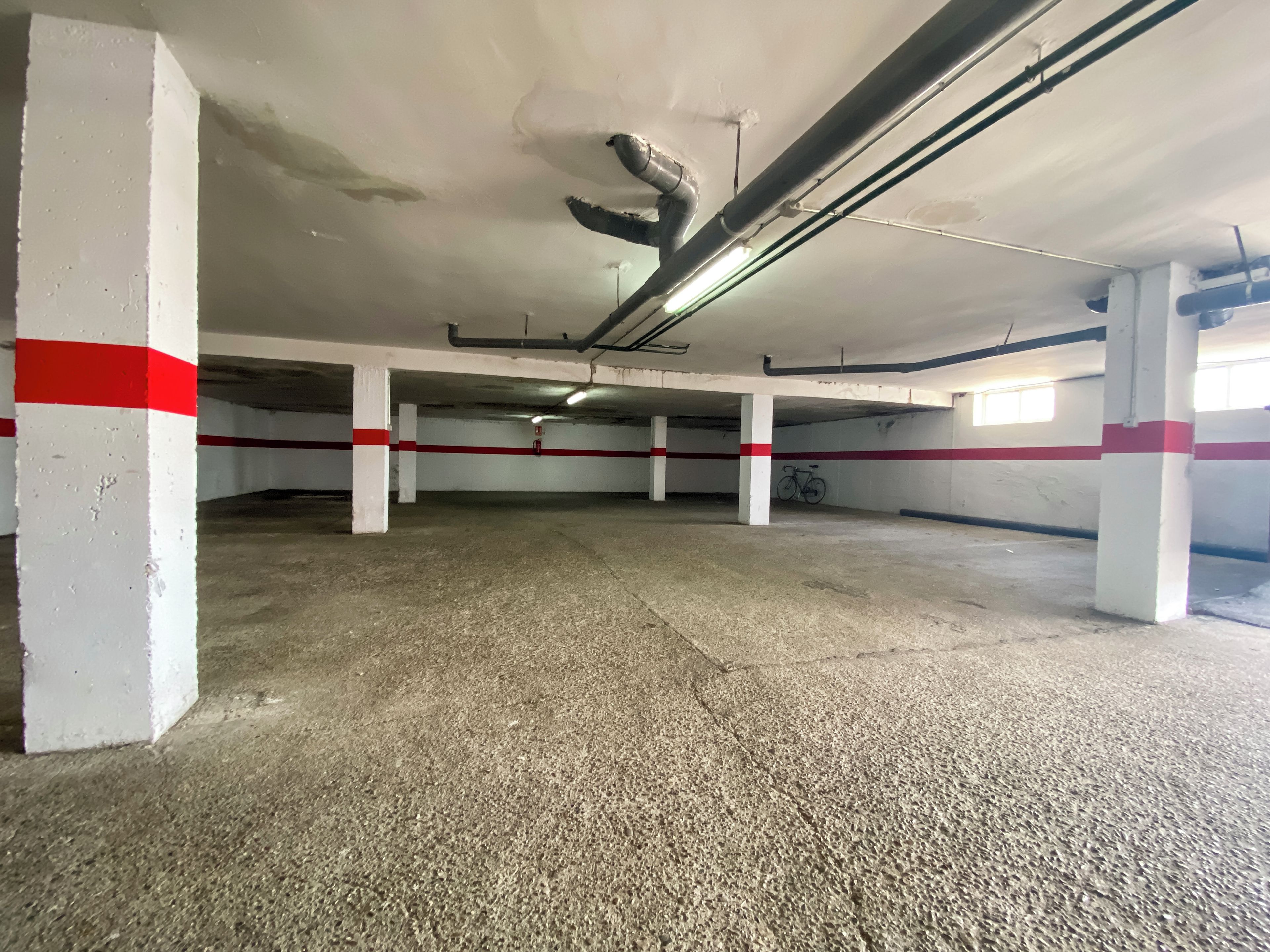 Een lege parkeergarage met betonnen vloeren en witte pilaren, gemarkeerd met rode strepen.