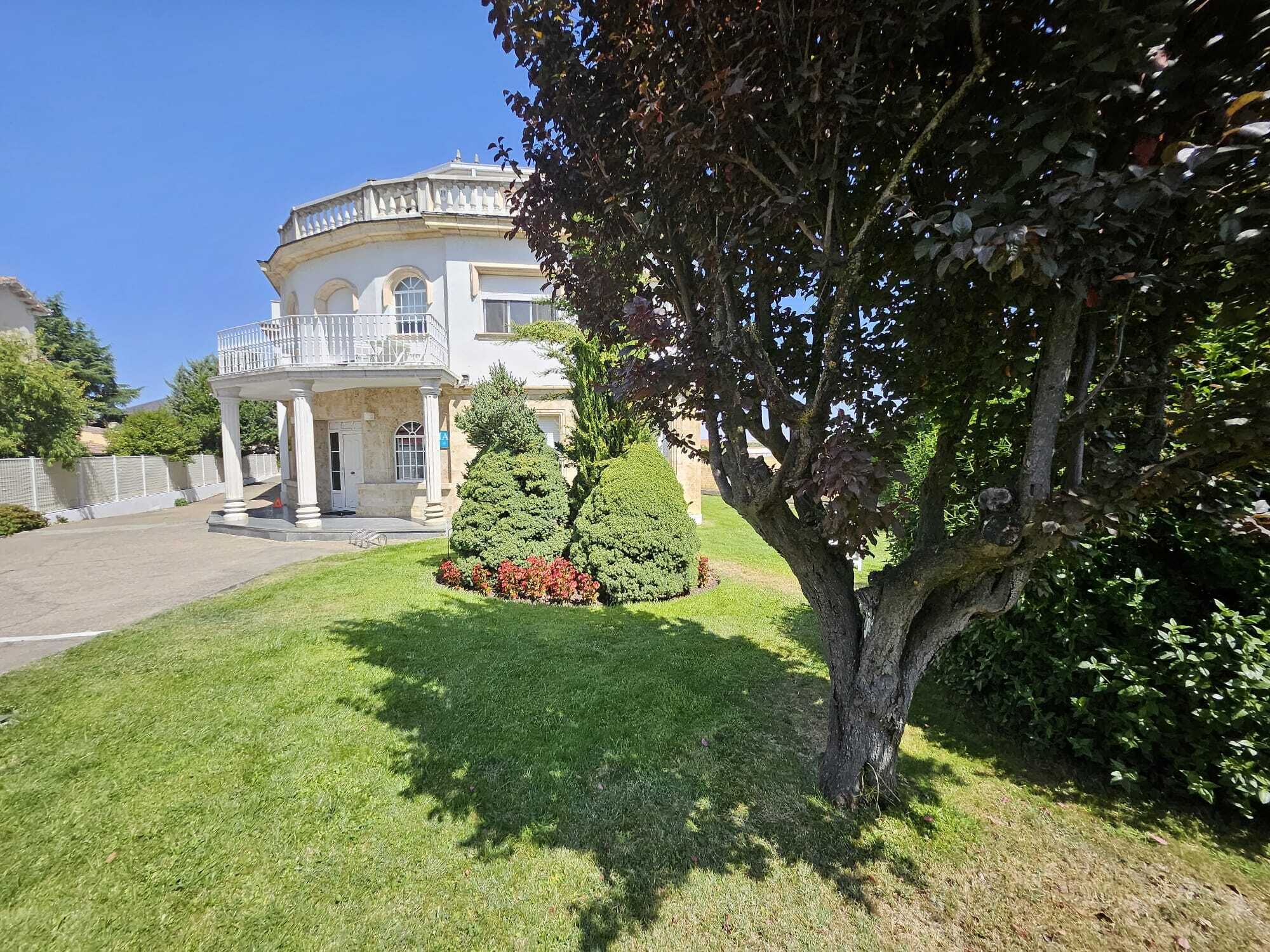 Ein großes, historisches Gebäude mit einer zentralen Kuppel, einer symmetrischen Fassade und einem gepflegten Rasen mit Baum und Sträuchern.
