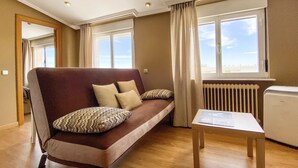 A modern living room with a brown sofa, beige cushions, a small white table, and a radiator. - Casablanca Hotel Studios (Santa Marta de Tormes)