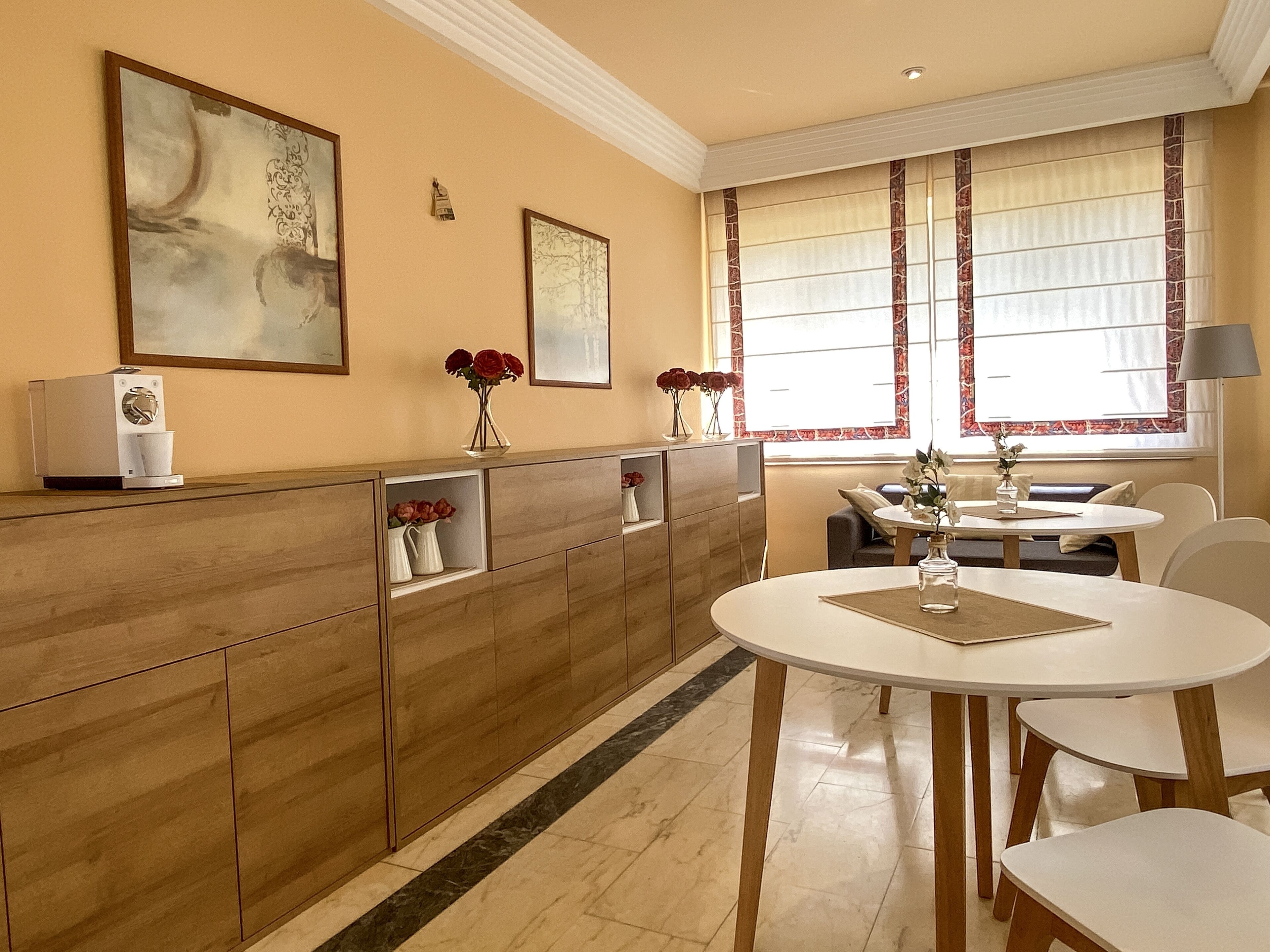 Una cocina moderna con cafetera integrada, una mesa de comedor con sillas y un ventanal con cortinas.
