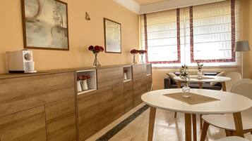 Una cocina moderna con cafetera integrada, una mesa de comedor con sillas y un ventanal con cortinas.