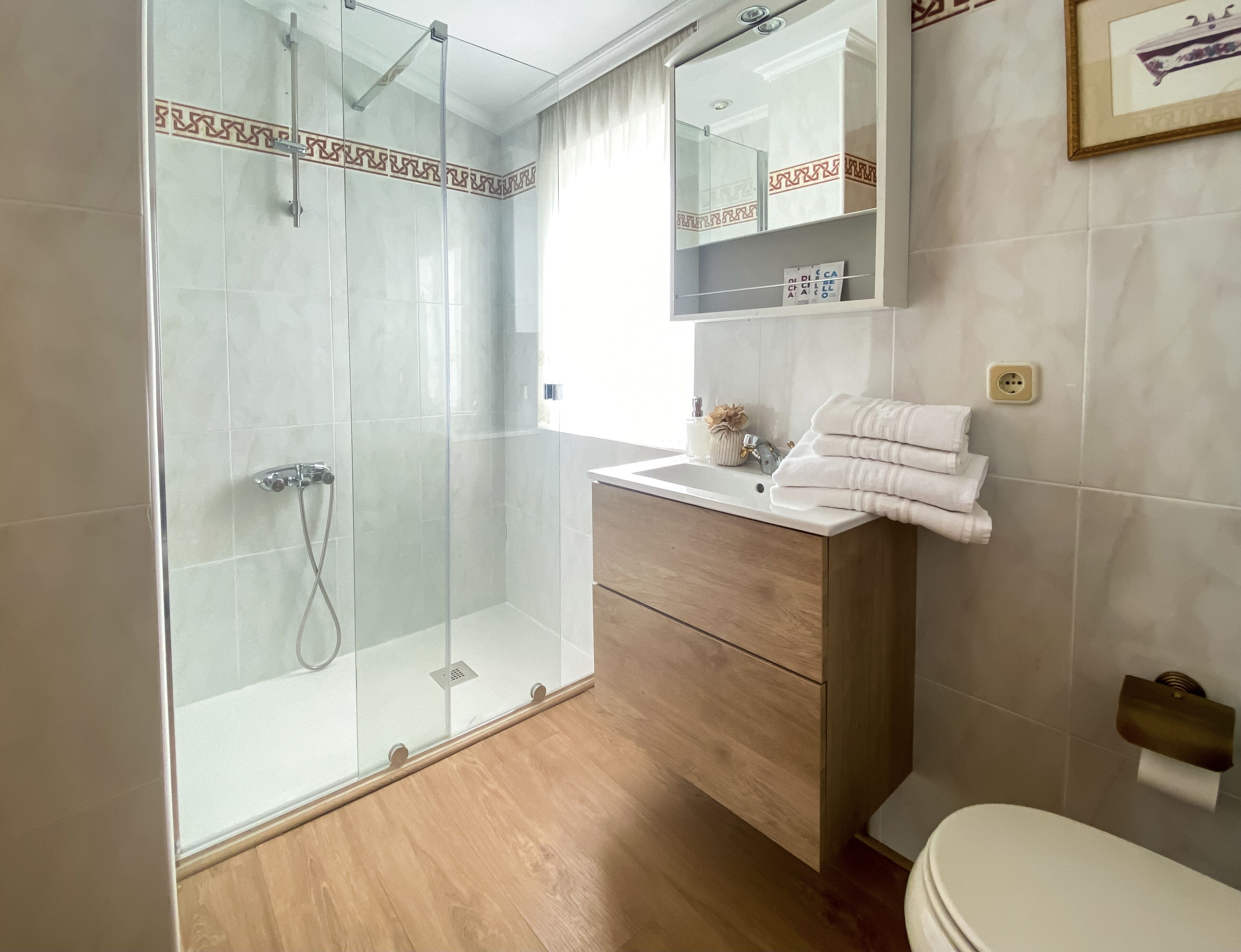 Un baño moderno con ducha de vidrio, tocador de madera con lavamanos y un inodoro.