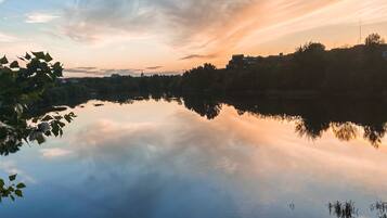 A calm lake reflecting the sky with trees and buildings in the background.