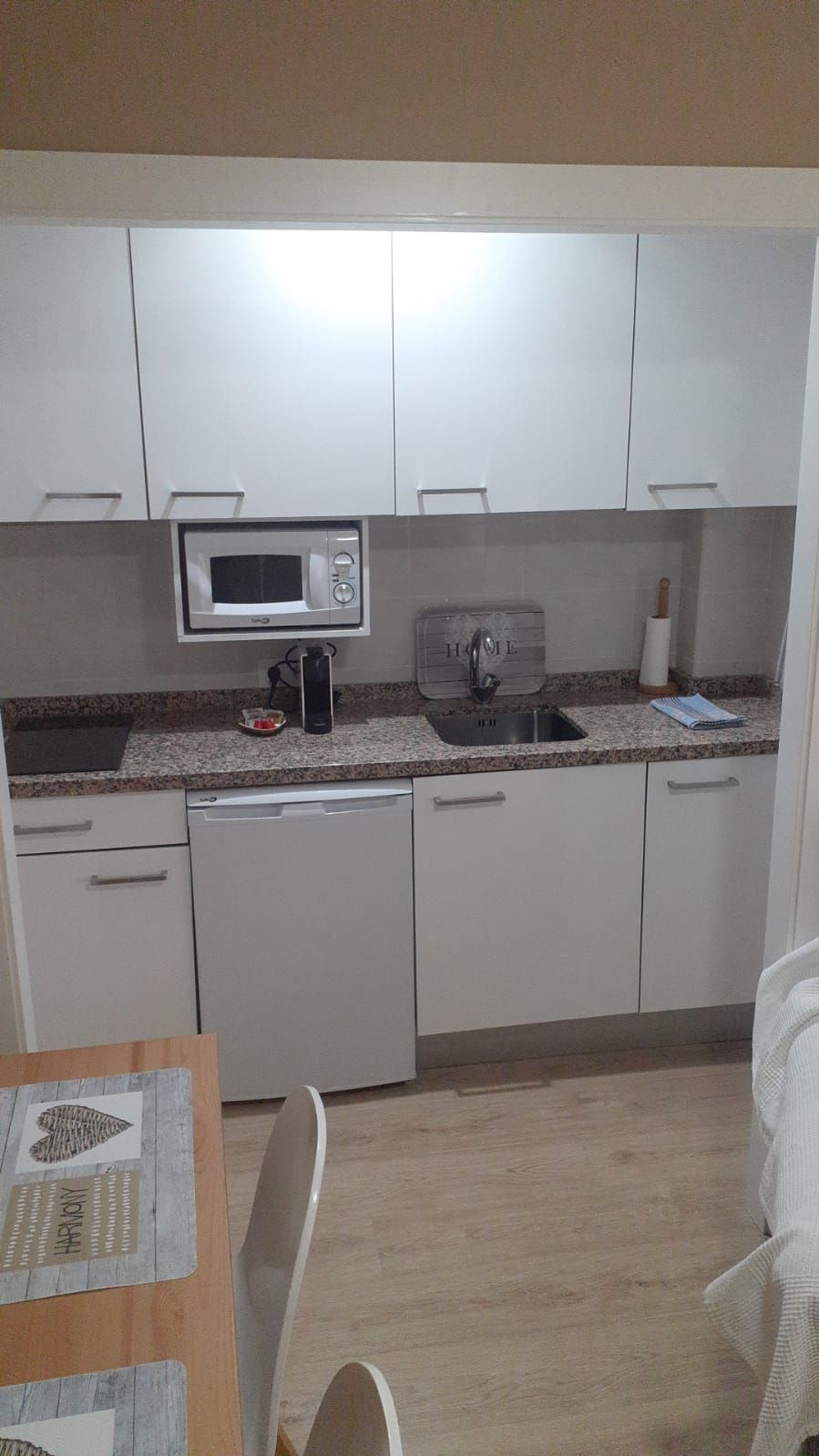 A compact kitchen with white cabinets, a microwave, a sink, and a small countertop.
