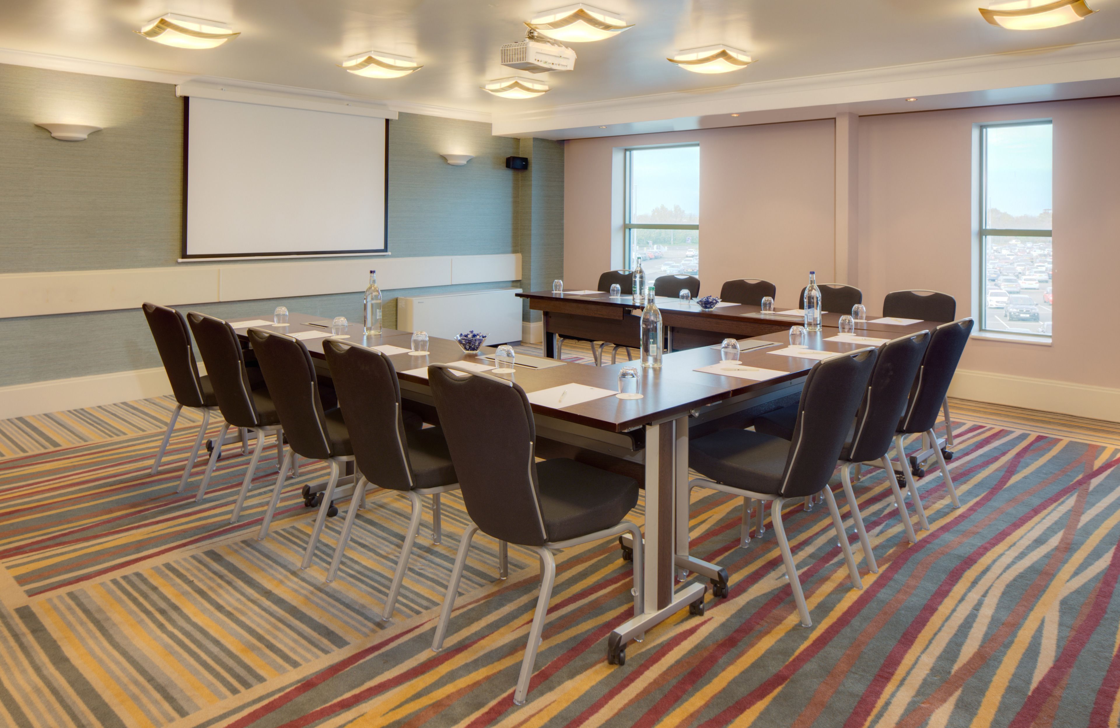 A conference room with a long table, chairs, a projector screen, and a large window.