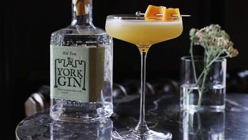 Una botella de ginebra Old Tom York y una copa de cóctel con un adorno de naranja sobre una mesa de mármol.