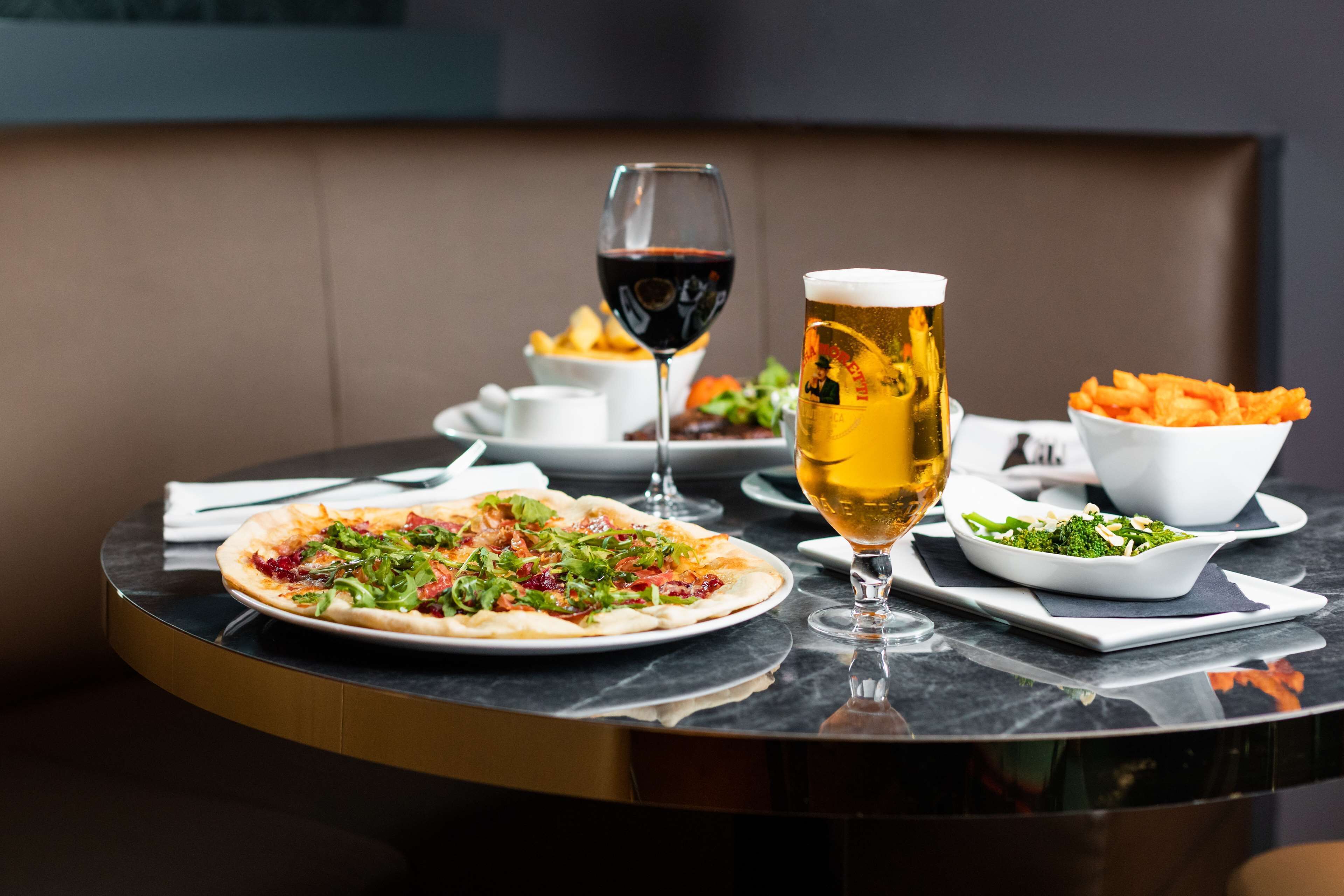 A dining table with a pizza, a glass of red wine, a glass of beer, and a bowl of fries.