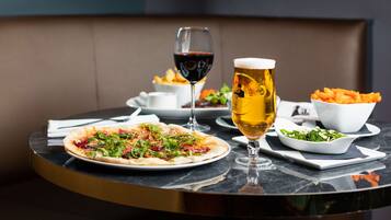 A dining table with a pizza, a glass of red wine, a glass of beer, and a bowl of fries.