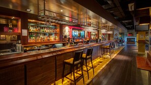 Um bar com um balcão comprido, vários taburetes e uma variedade de garrafas e copos.