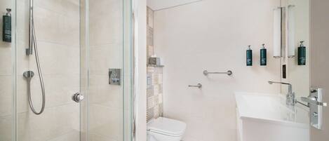 A modern bathroom with a glass-enclosed shower, a white toilet, and a sink with a mirror.