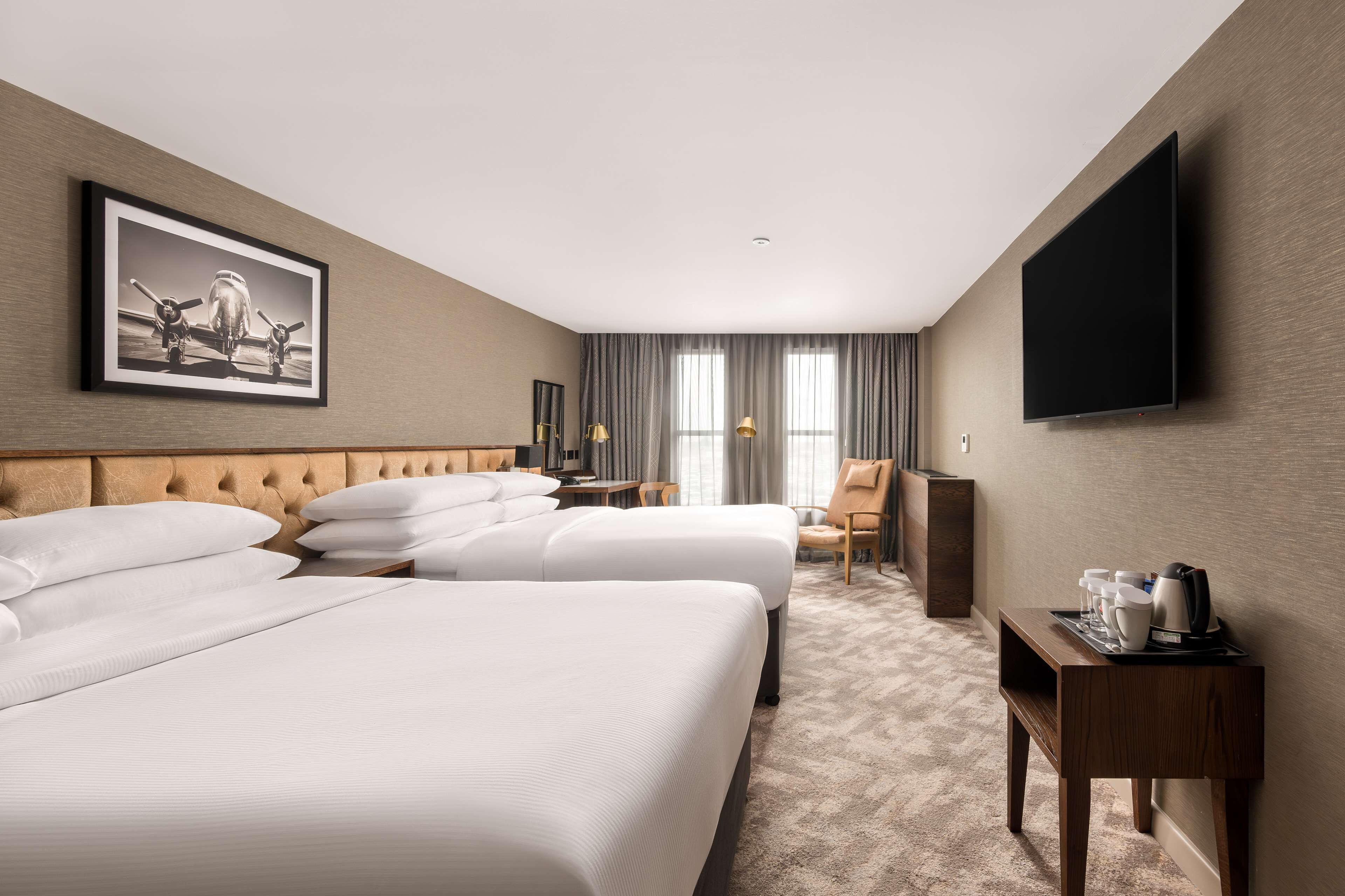 A hotel room with two beds, a flat-screen TV, a framed picture on the wall, a small table with a tray, and a chair.