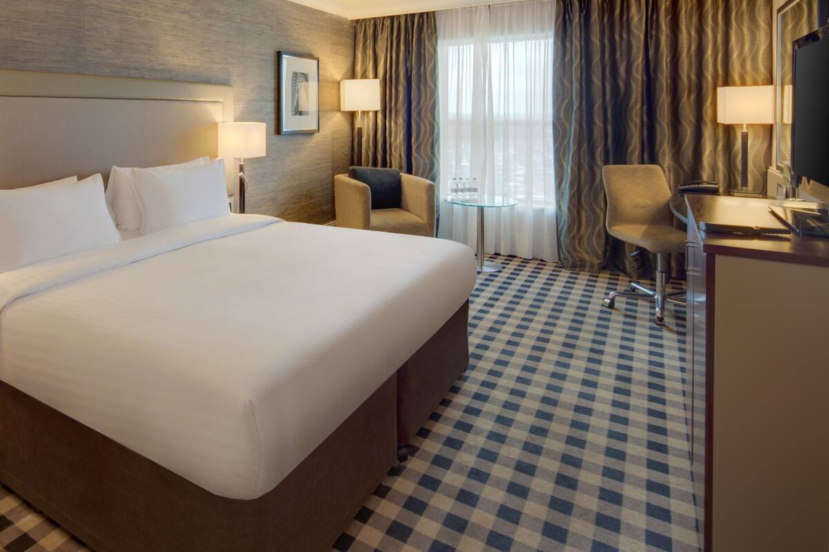 A hotel room with a large bed, a desk, a chair, and a television.