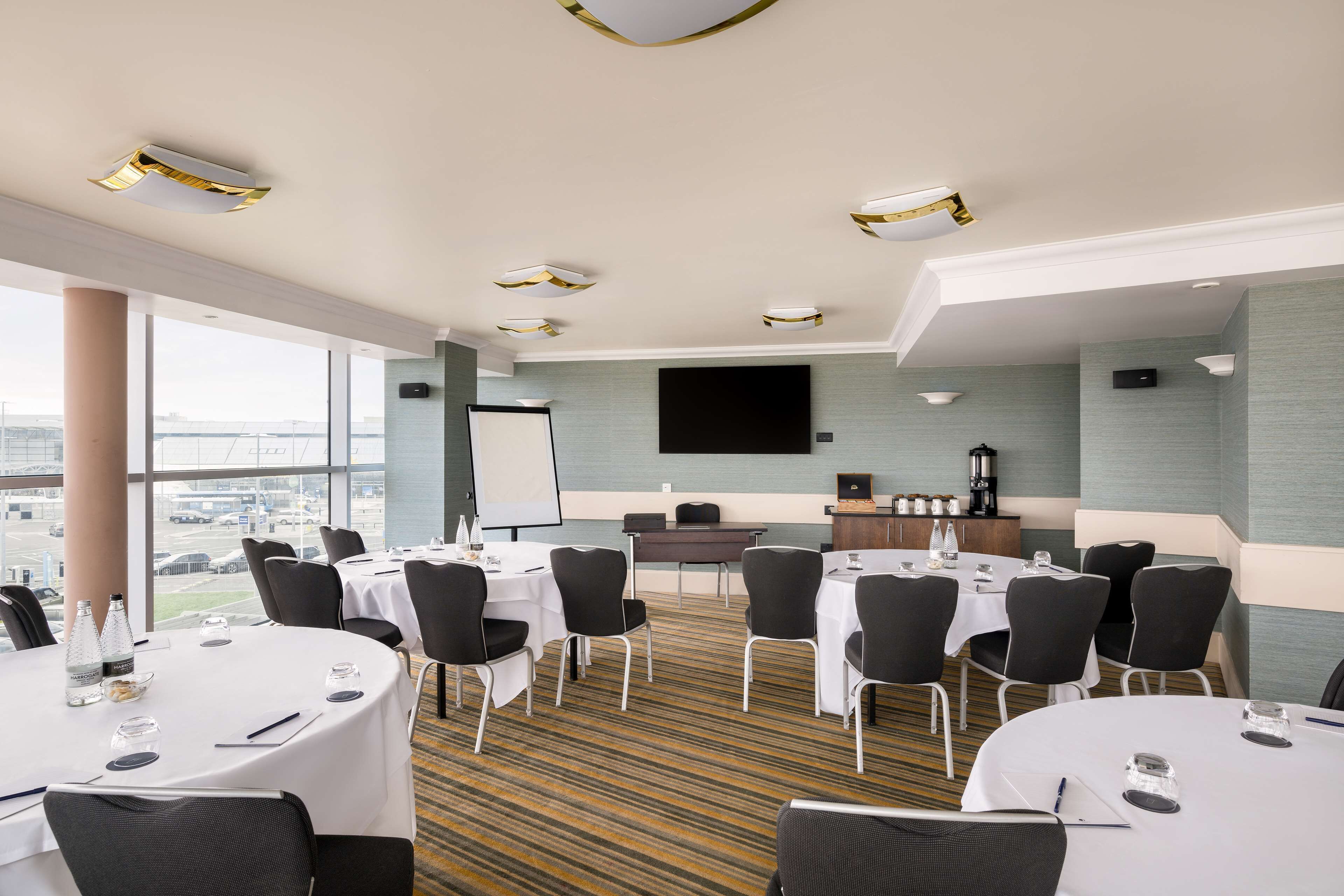 A conference room with round tables, black chairs, a whiteboard, and a large window with a view of the city.
