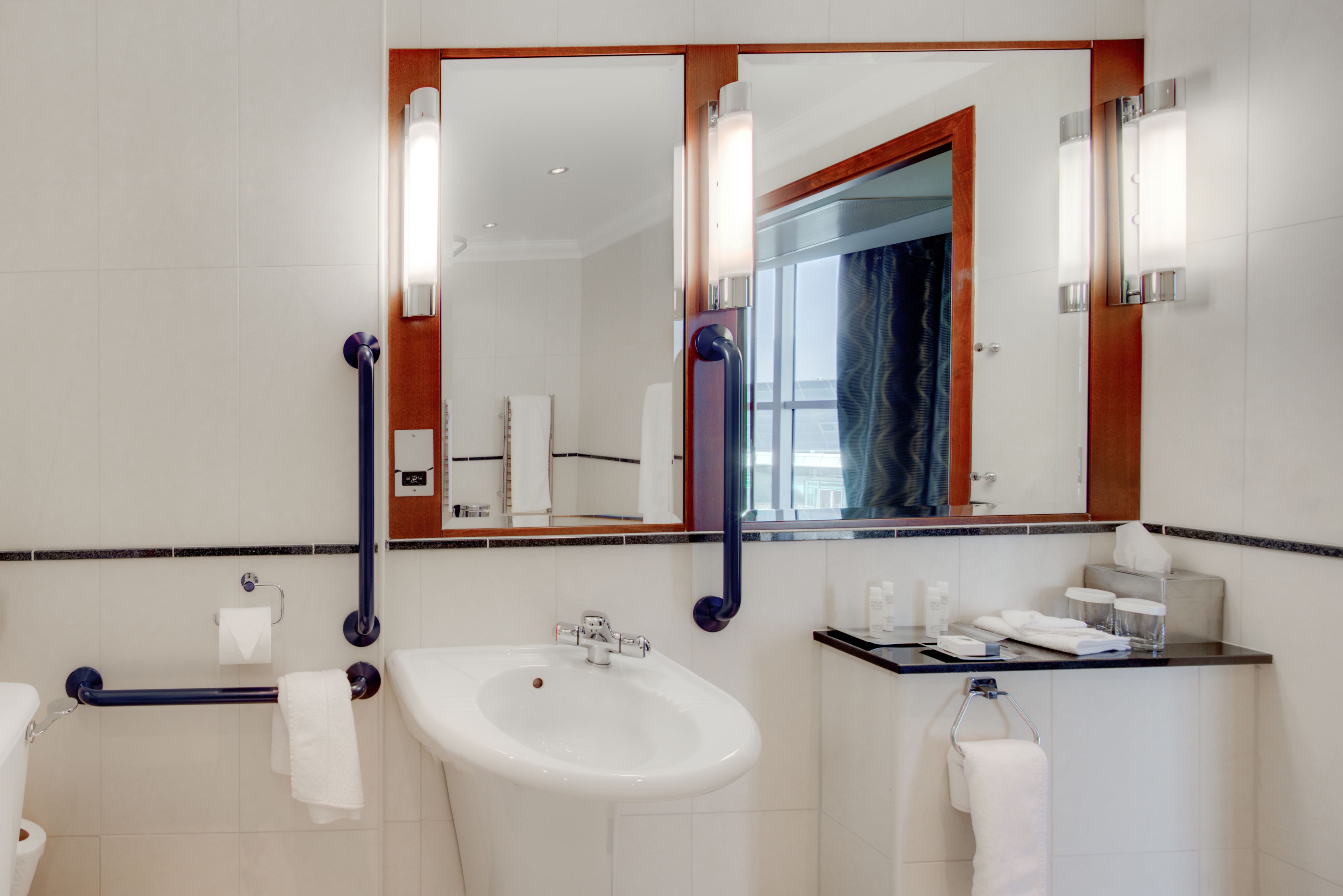 Un baño moderno con lavamanos, espejo y toallero blancos.