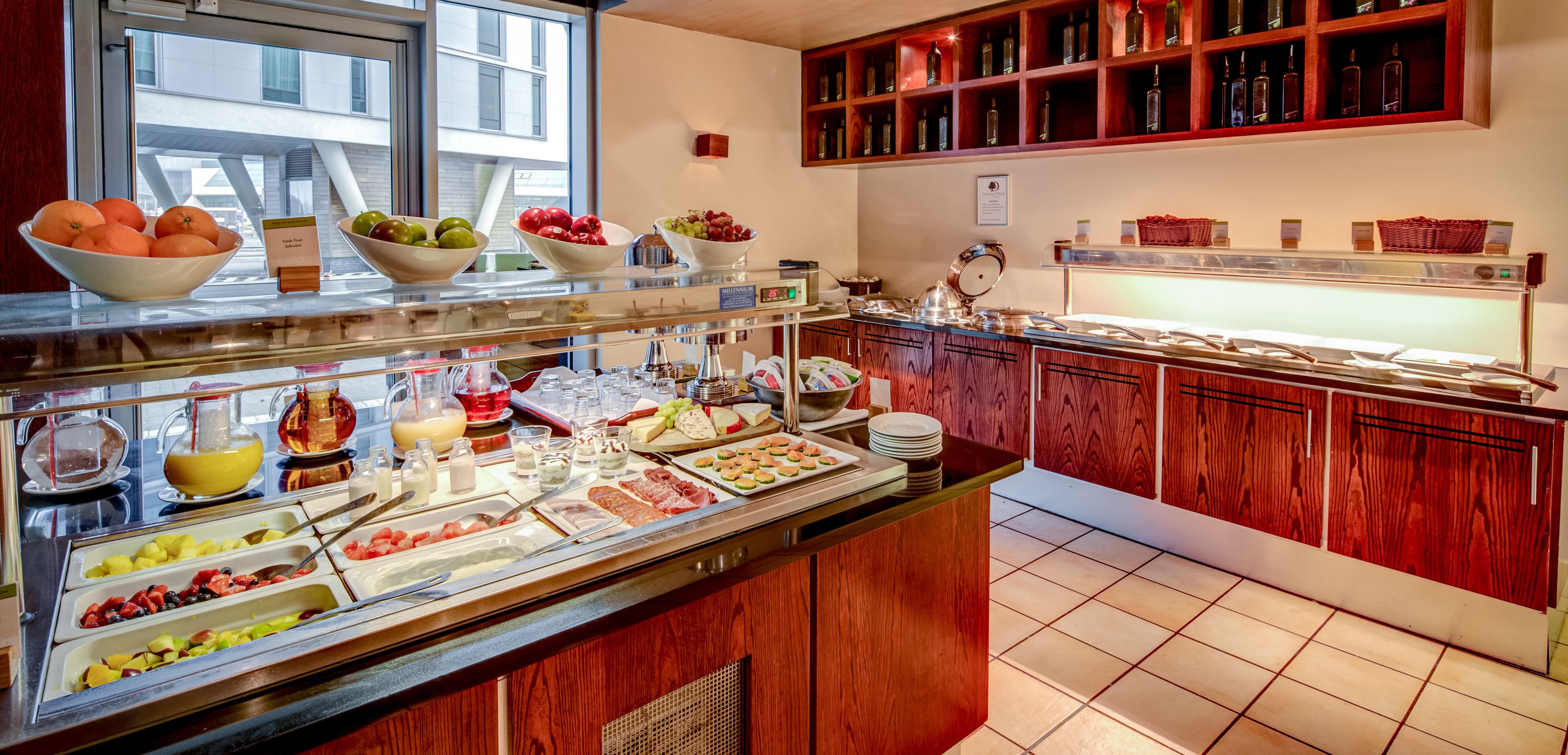 Un bufé con diversos alimentos y una estantería de vinos.