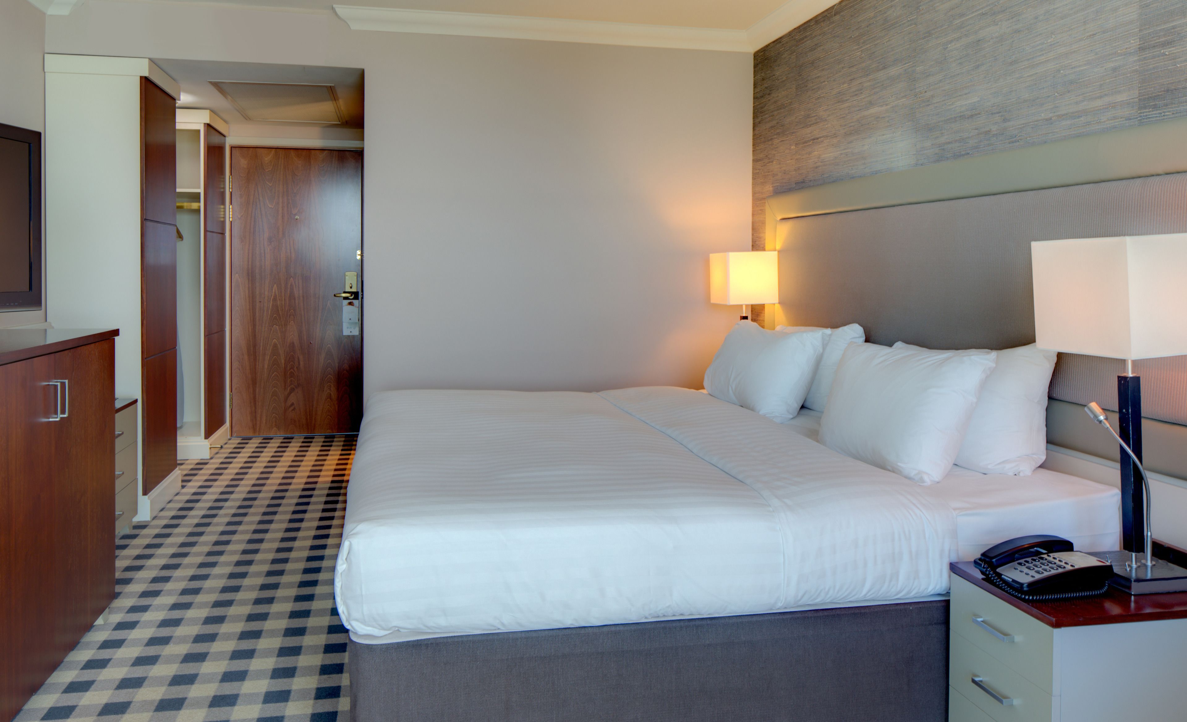 A hotel room with a large bed, bedside lamp, and a telephone on the nightstand.