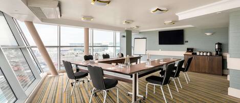 A conference room with a large table, chairs, a projector screen, and a kitchen area.