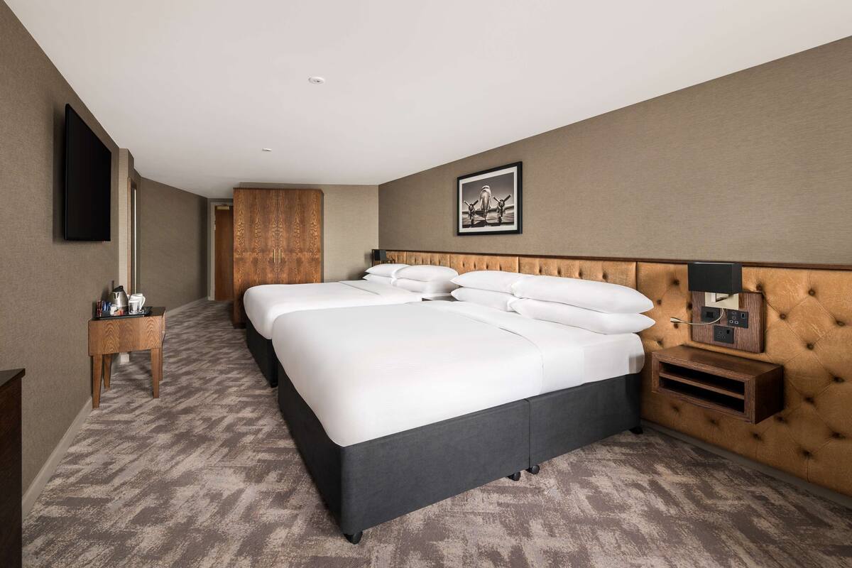 A hotel room with a large bed, a bedside table, a TV mounted on the wall, and a framed picture above the bed.